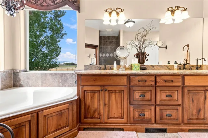 Built-in soaking tub with tiled surround, wood-finish cabinetry, dual vanity with undermount sinks, and broad mirrors