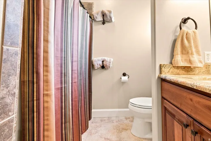 Warm-toned vanity with stone countertop, tile flooring, and integrated toilet