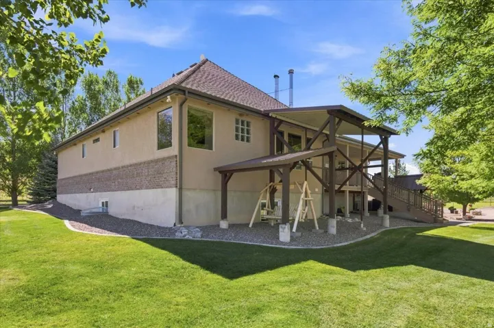 Expansive exterior featuring stucco siding, a brick accent band, a covered upper-level deck, and a lower-level patio