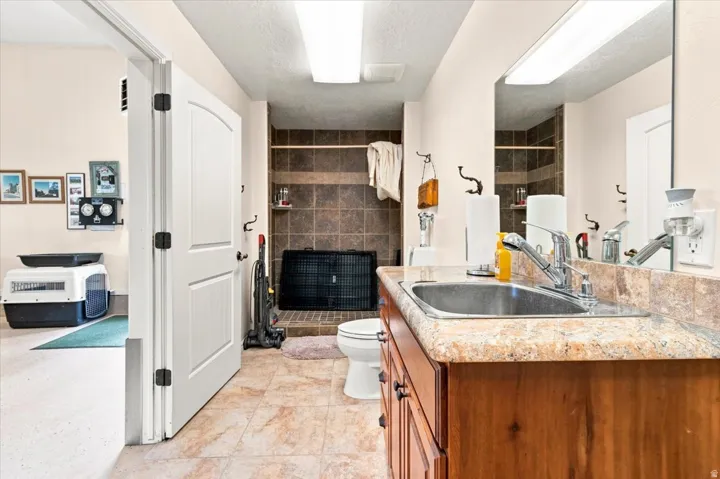 Functional utility space featuring a stainless steel sink, wood-finish cabinetry, tiled flooring, and a tiled shower area
