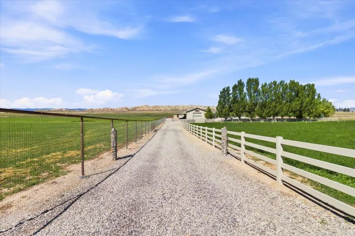 Gravel driveway with a white split-rail fence, leading to a distant building