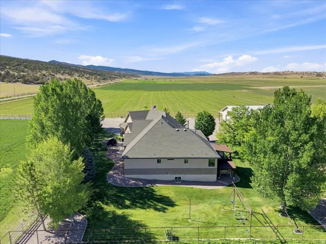 Property featuring a multi-level structure with a gabled roof and covered patio, surrounded by mature trees and manicured lawns, with distant mountains and fields