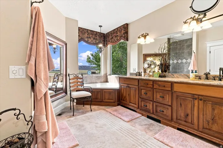 Corner soaking tub, dual vanity with undermount sinks, wood-finish cabinetry, and tiled flooring