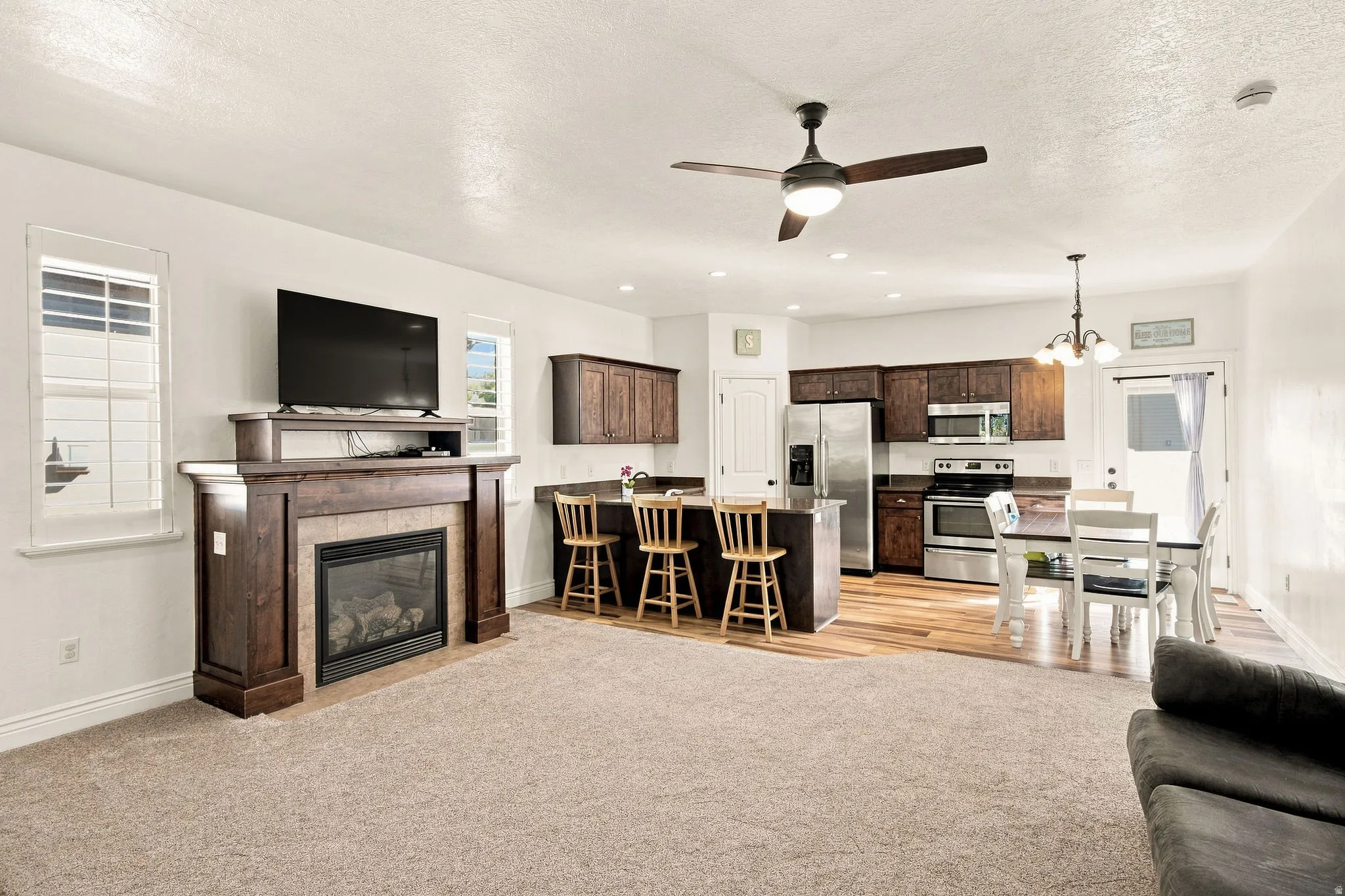 Living space and kitchen featuring a tiled fireplace with wood mantel, a kitchen island, dark wood cabinetry, LVP flooring and stainless steel appliances