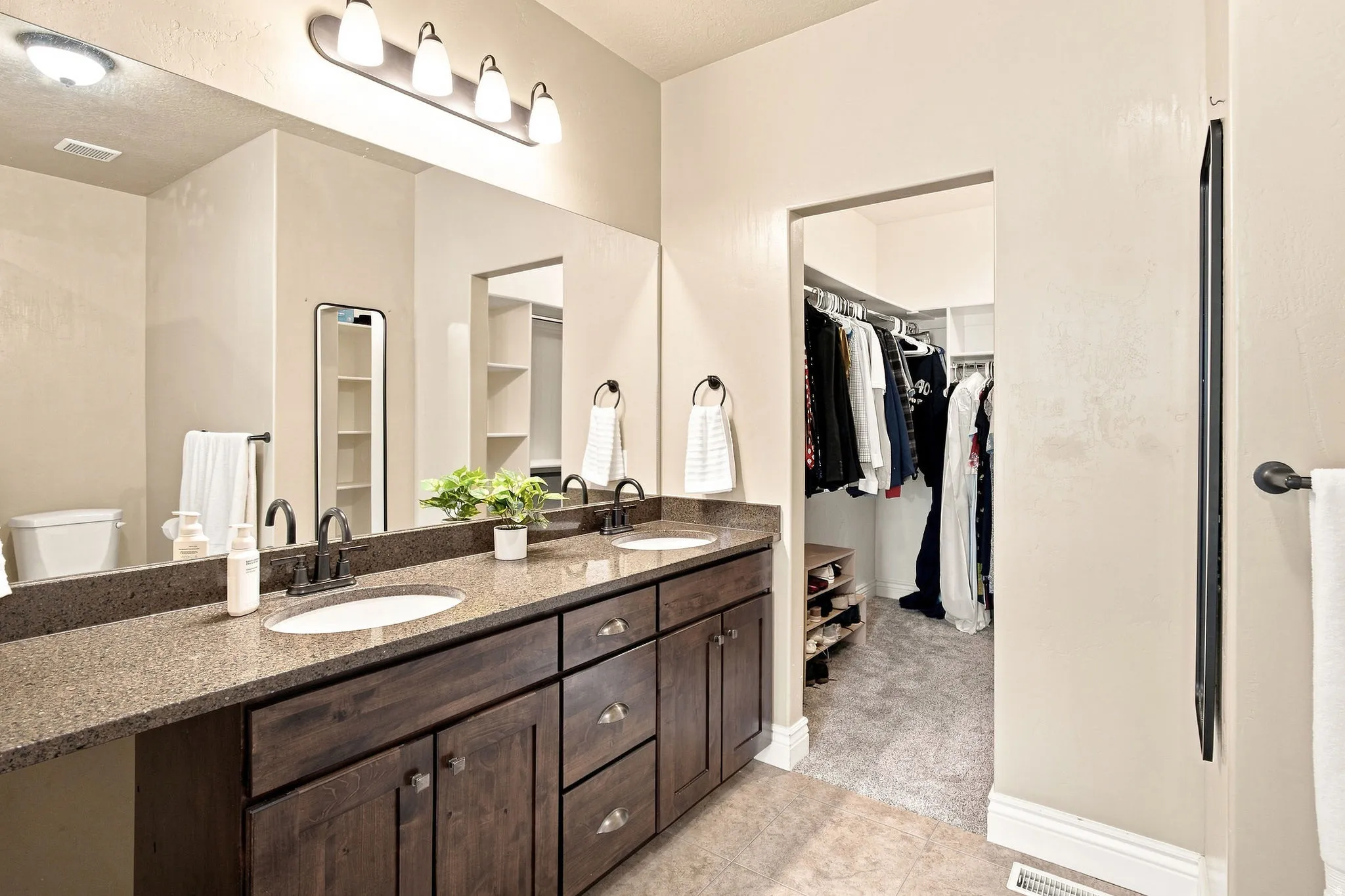 Double vanity with a granite countertop and dark wood-finish cabinetry and walk-in closet