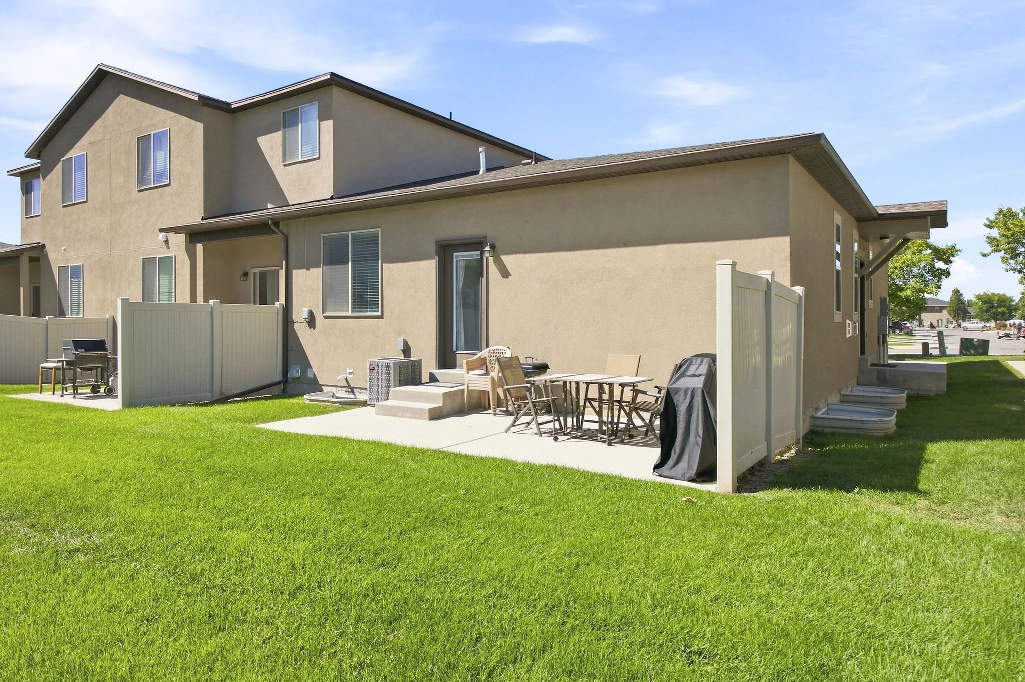 Expansive green lawn, stucco exterior, rear patio, privacy fencing, and exterior steps