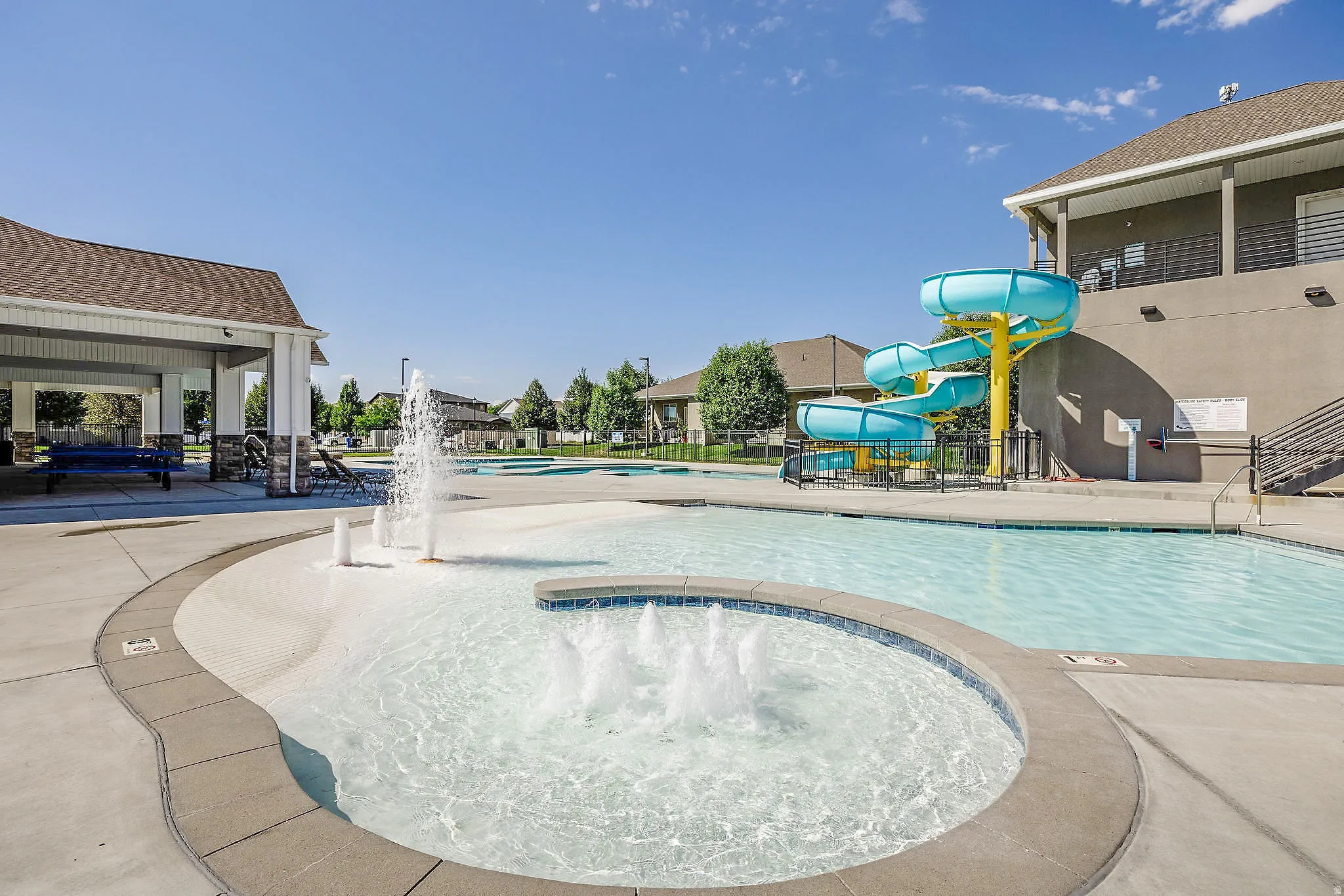 Expansive pool area featuring a water slide, multiple water features, and a covered pavilion