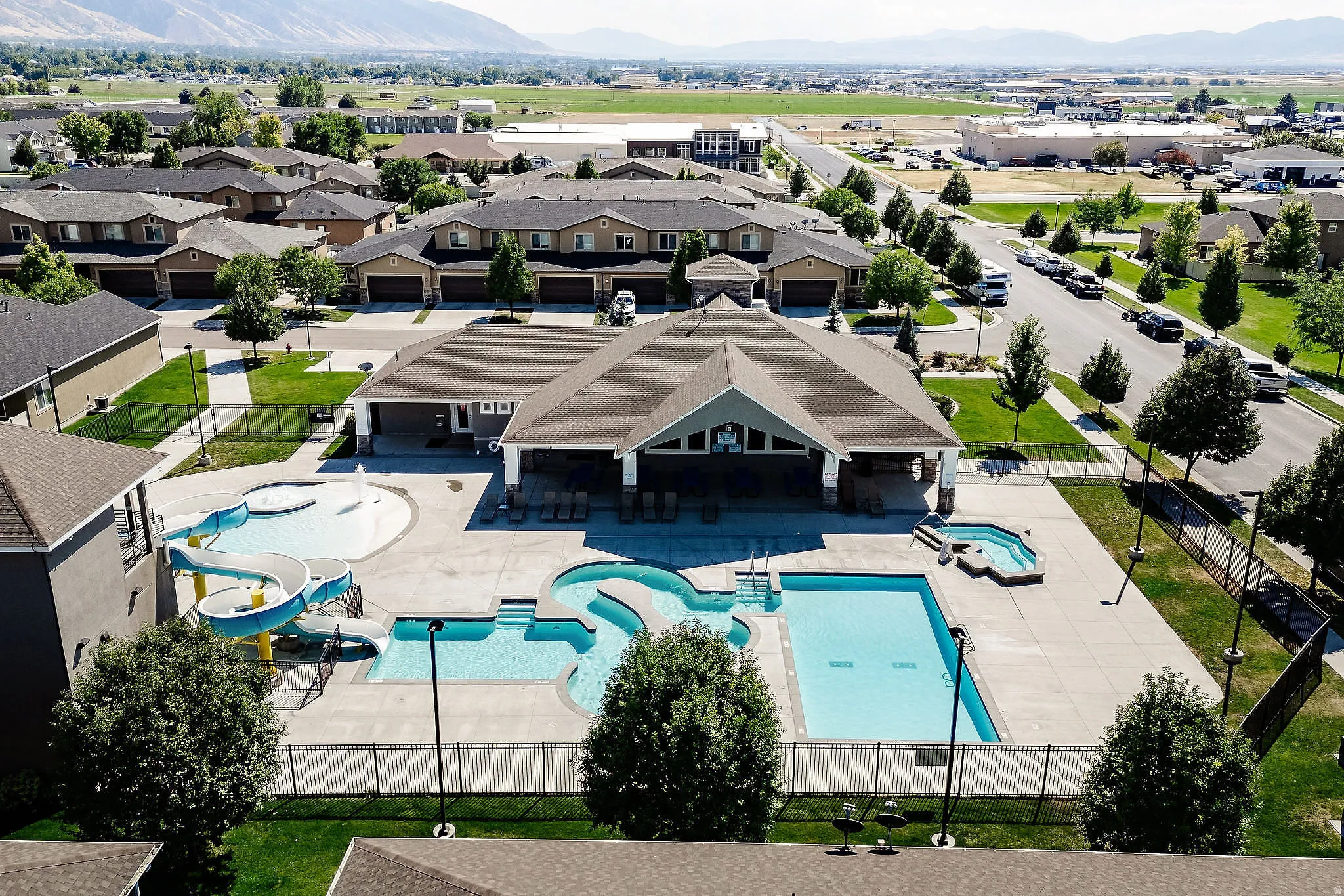 Central community building featuring a large gabled roof, an expansive pool deck, and a multi-level swimming pool with a water slide