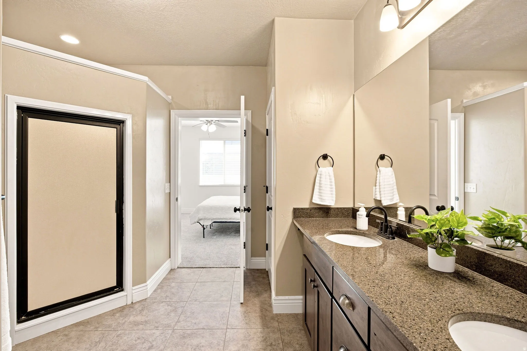 Double vanity with integrated sinks, shower, dark wood-finish cabinetry, and a granite countertop