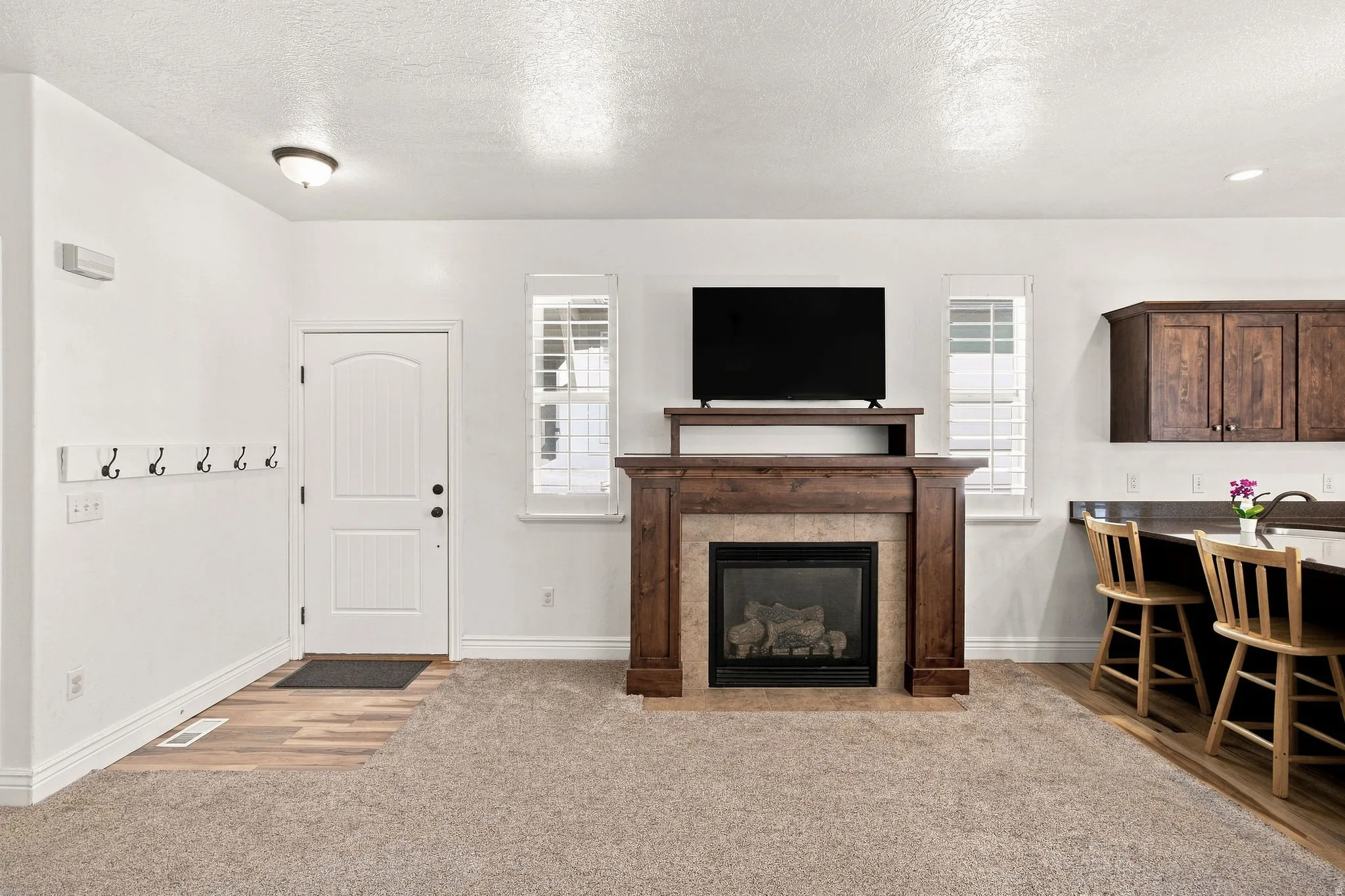 Wood-finish flooring entry, living area, leading to a fireplace with a wood and stone mantle.