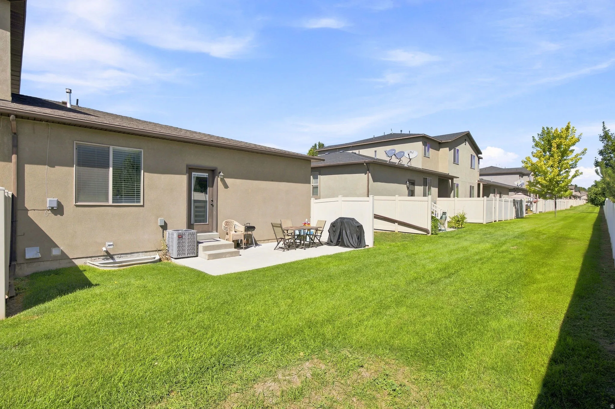 Expansive green lawn with a concrete patio, vinyl fencing, and mature trees