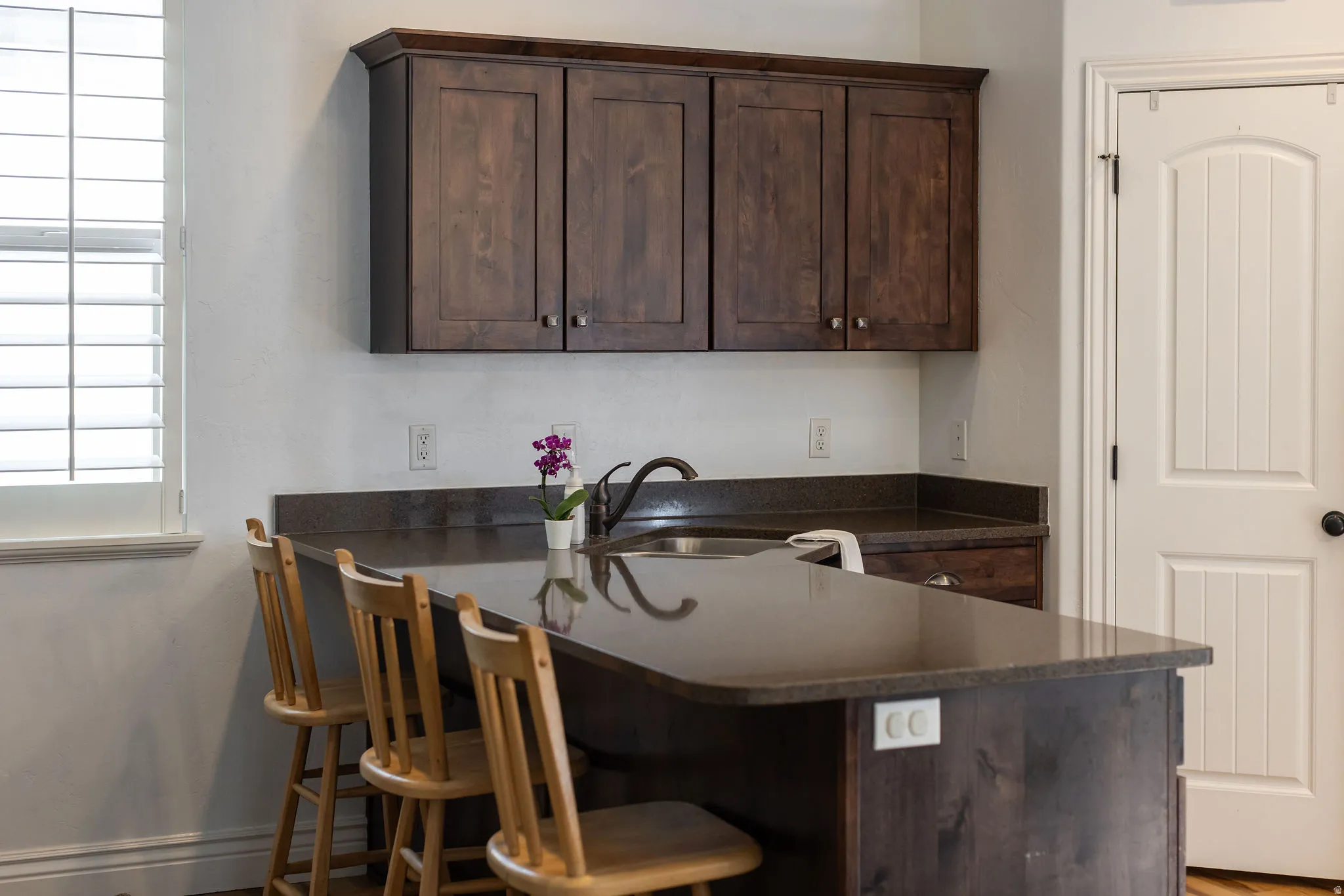 Kitchen featuring wood-finish cabinetry, dark countertops, a stainless steel sink, and plantation shutters