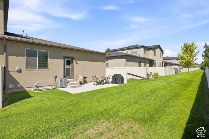 Expansive green lawn with a concrete patio, vinyl fencing, and mature trees