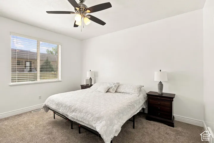 Primary bedroom featuring a ceiling fan with integrated lighting, carpet flooring, and window with horizontal blinds