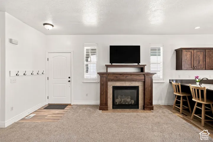 Wood-finish flooring entry, living area, leading to a fireplace with a wood and stone mantle.