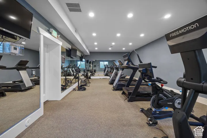 Cardio fitness area featuring mirrored walls, recessed lighting, and carpet flooring