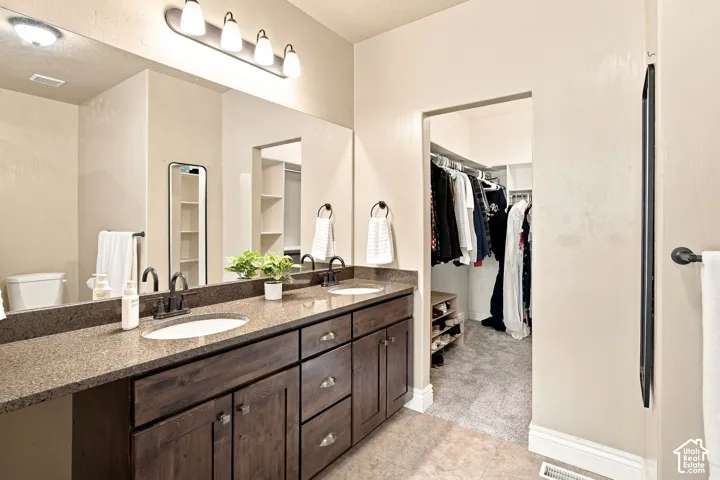 Double vanity with a granite countertop and dark wood-finish cabinetry and walk-in closet