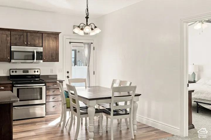 Kitchen featuring wood-finish flooring, stainless steel appliances, dark wood cabinetry, and a ceiling-mounted chandelier