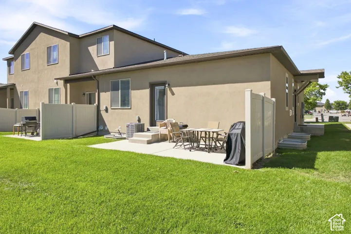 Expansive green lawn, stucco exterior, rear patio, privacy fencing, and exterior steps