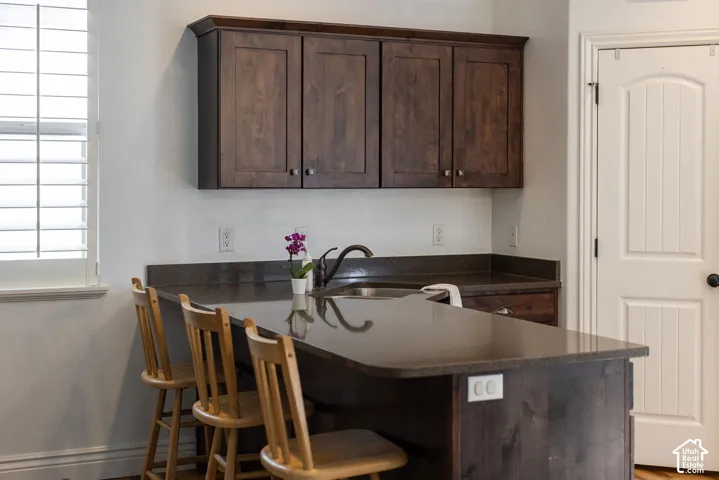 Kitchen featuring wood-finish cabinetry, dark countertops, a stainless steel sink, and plantation shutters
