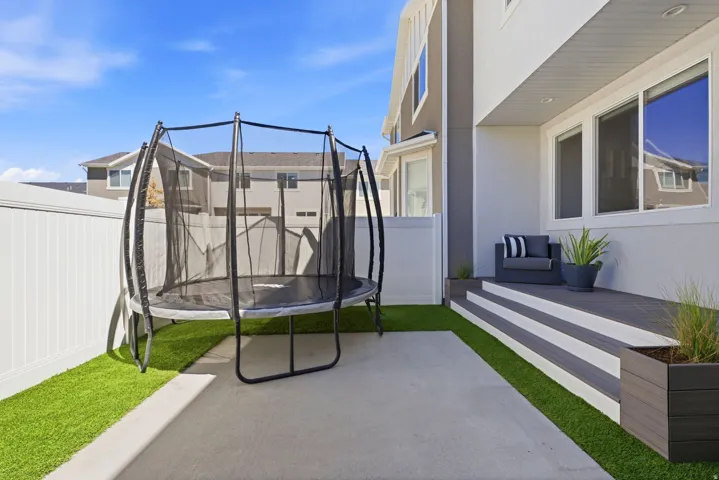 Paved patio area featuring artificial turf accents, white privacy fencing, and a multi-level composite deck with integrated planter boxes