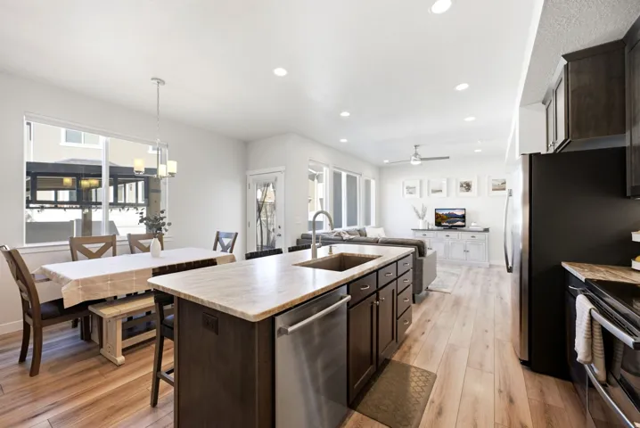 Open-concept layout with wood-finish flooring, kitchen island with stone countertop, stainless steel dishwasher, and recessed lighting
