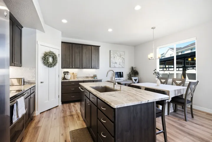 Kitchen featuring wood-finish flooring, dark wood cabinetry, light-toned countertops, a center island with an integrated sink, and an undermount sink with a gooseneck faucet