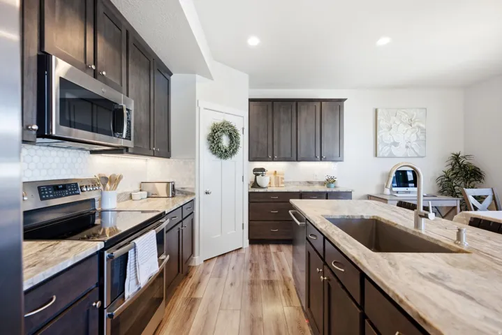 Kitchen featuring wood-finish flooring, dark wood cabinetry, stainless steel appliances, a tile backsplash, and light-toned countertops