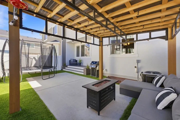 Covered patio featuring a wood beam and metal roof structure, concrete patio, artificial turf, and a built-in fire pit