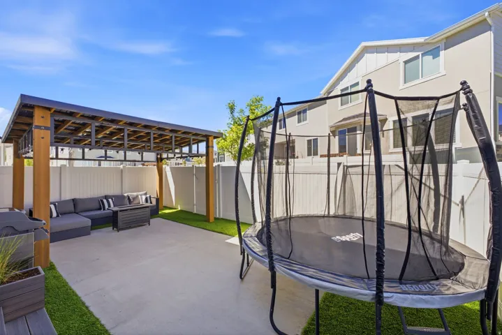 Backyard featuring a concrete patio, artificial turf, and a wood-beamed pergola