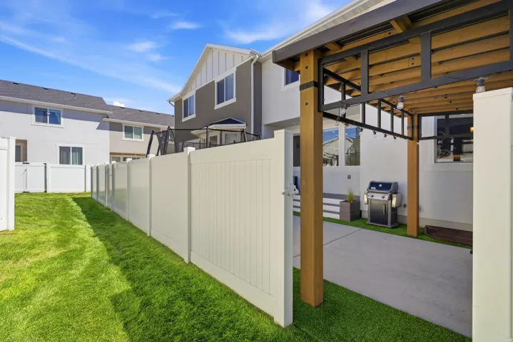 Side yard with white privacy fencing, natural grass, and a paved patio area