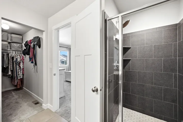 Walk-in closet with built-in shelving, shower with dark rectangular wall tiles, and white hexagonal floor tiles