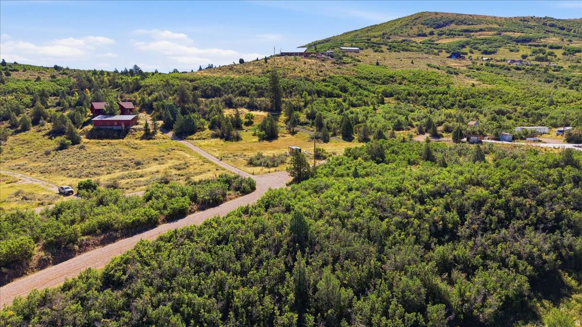 Expansive property featuring a winding dirt road, scattered structures, and natural, undulating terrain