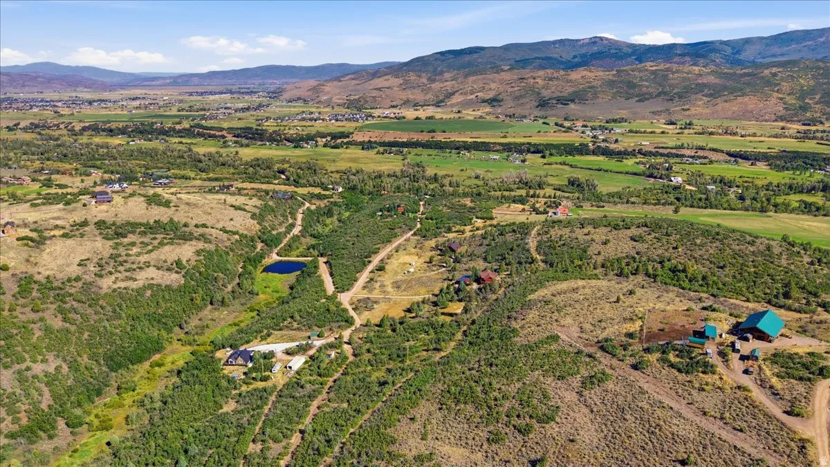Expansive property featuring varied terrain, multiple structures, a private pond, and mountain backdrops