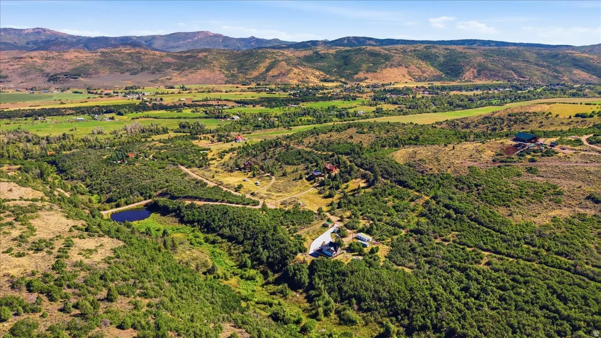 Expansive natural landscape featuring rolling hills, abundant green foliage, a prominent body of water, and distant mountain ranges