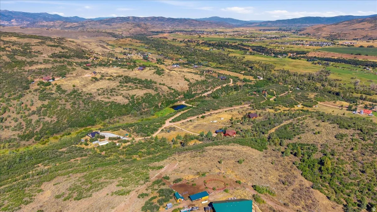 Expansive terrain with mountain backdrop, featuring varying natural vegetation and a visible pond