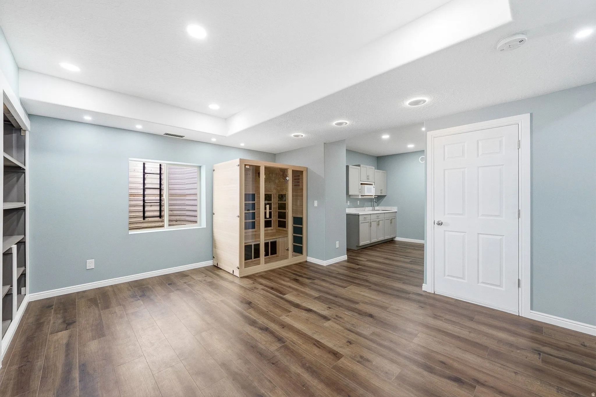 Recessed lighting, wood-finish flooring, built-in shelving, egress window, and a kitchenette with light gray cabinetry