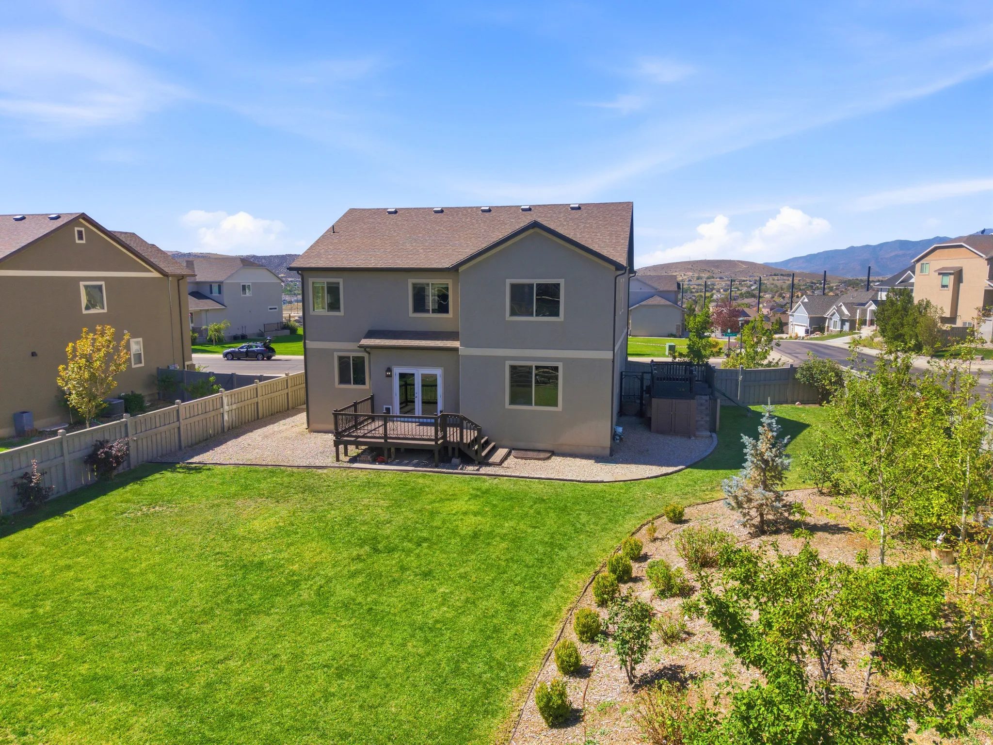 Expansive backyard featuring a manicured lawn, a built-in deck, and established landscaping