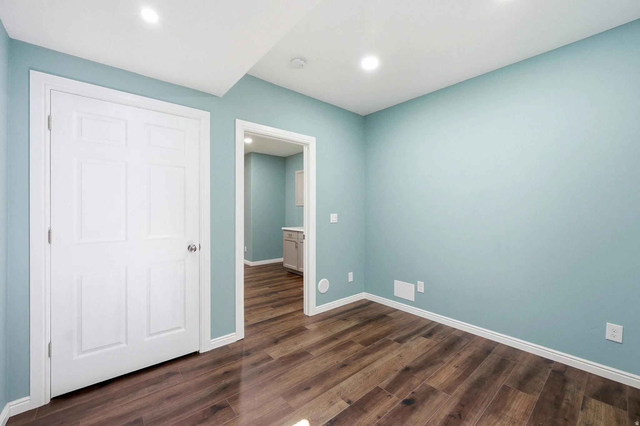 Wood-finish flooring, recessed ceiling lighting, light blue wall paint, white trim, and white paneled doors
