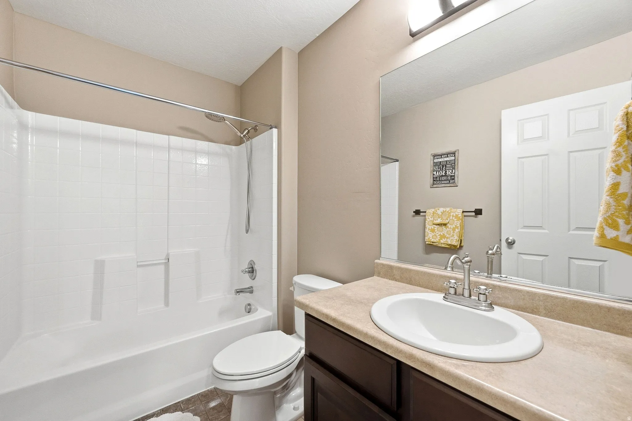 Bathroom featuring a white tub/shower combination, a vanity with a light-toned countertop, an oval undermount sink, and a framed mirror