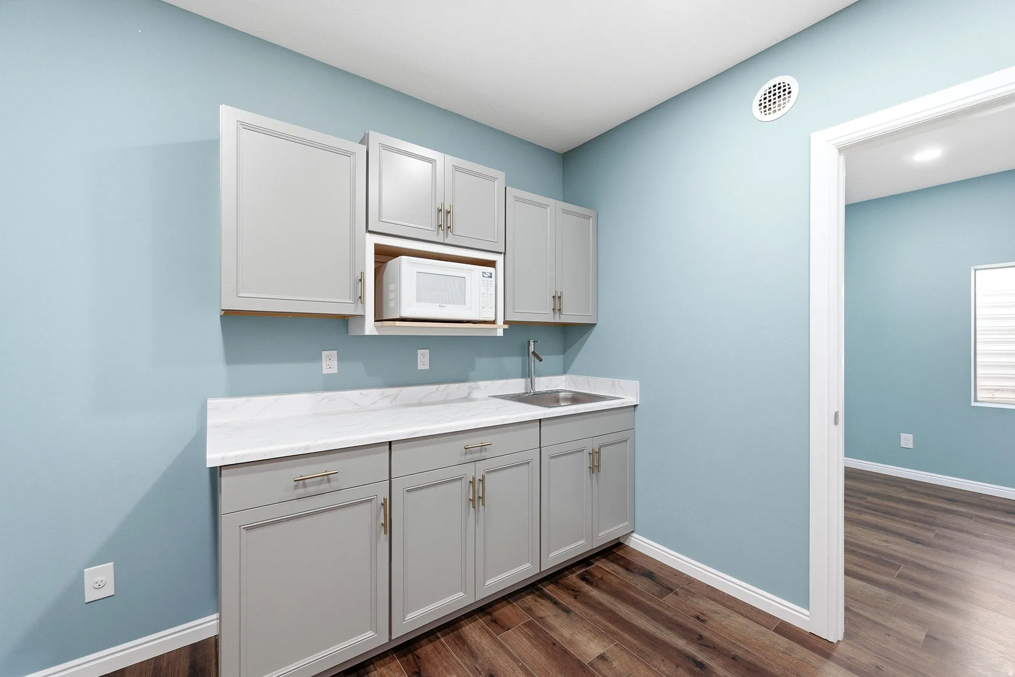 Compact kitchenette featuring gray cabinetry, a stainless steel sink, white countertop, and wood-finish flooring