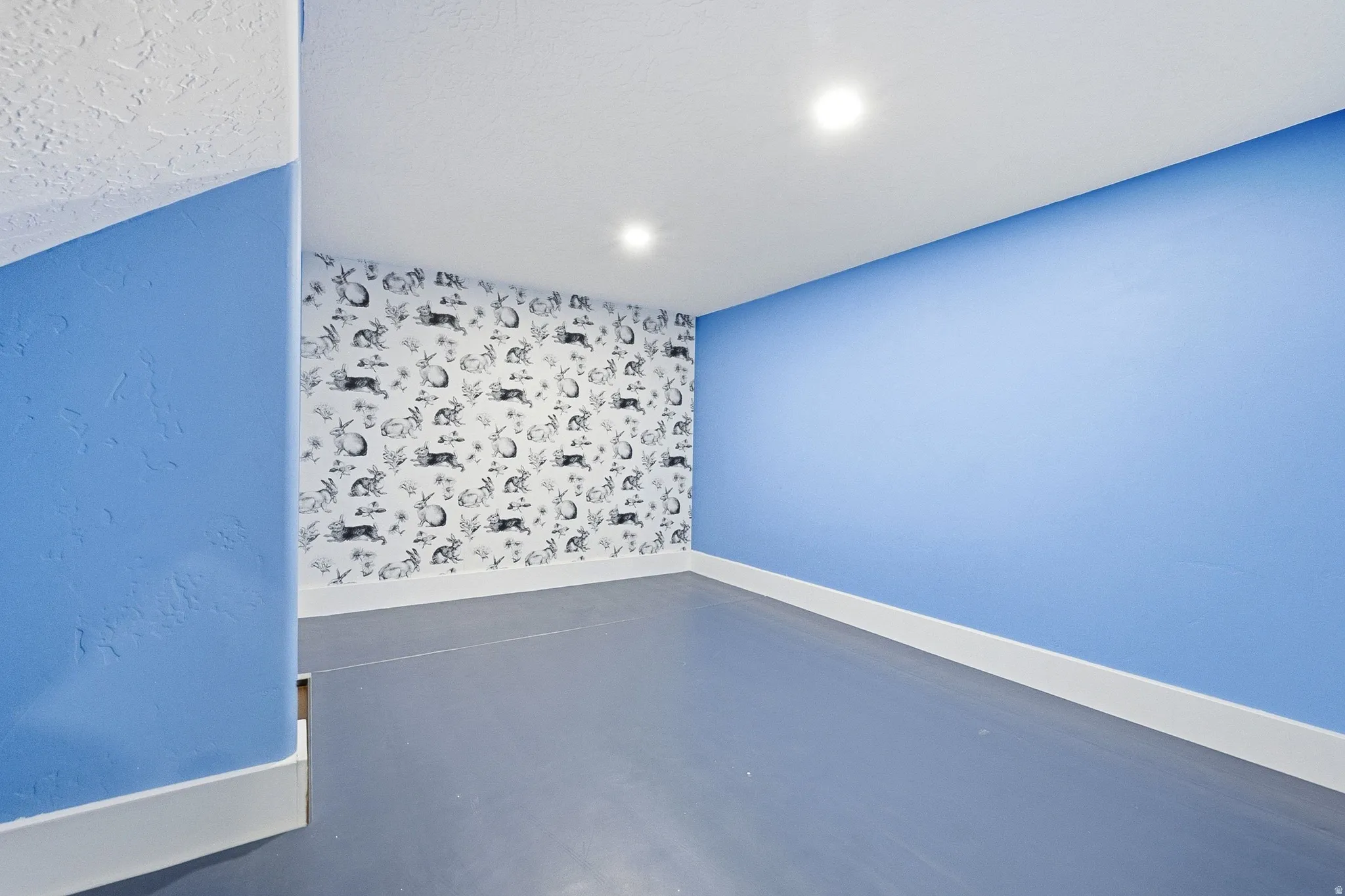 Textured wall finish, recessed lighting, accent wall with decorative wallpaper, light-colored trim, and light blue walls