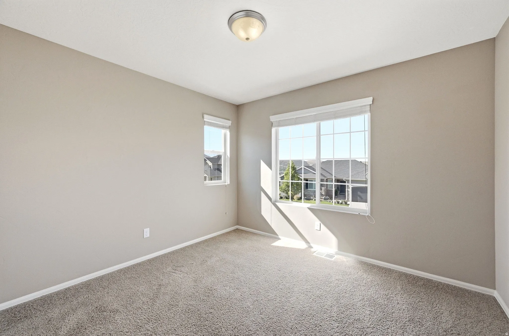 Neutral wall finishes, textured carpeting, large window with blinds, and flush-mount ceiling light