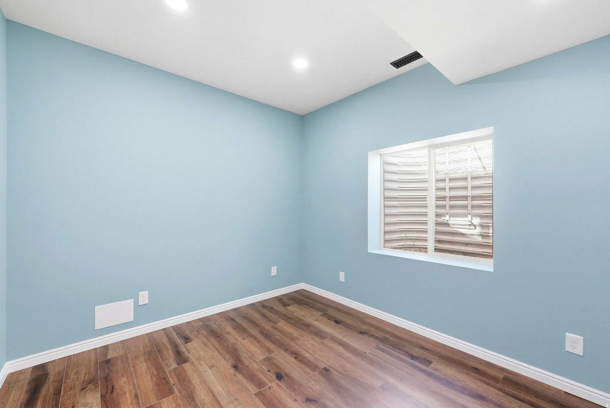 Recessed lighting, light blue walls, wood-finish flooring, white trim, and a window well