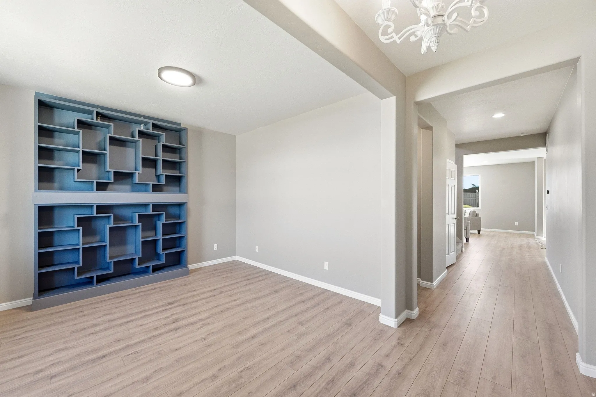 Built-in shelving unit, wood-finish flooring, recessed lighting, chandelier, and a bright interior