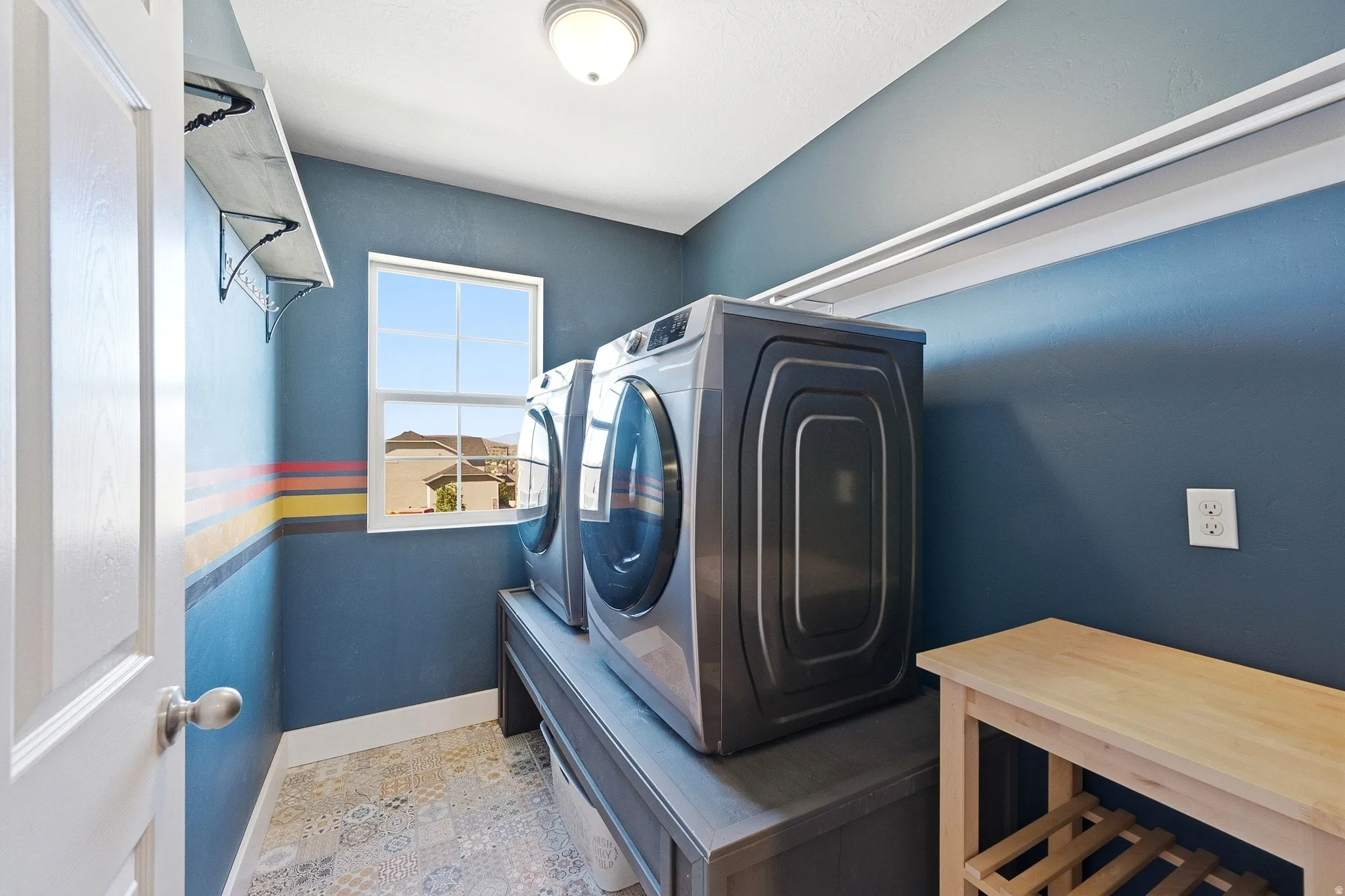 Laundry area featuring a window, patterned tile flooring, and a built-in shelf with decorative brackets