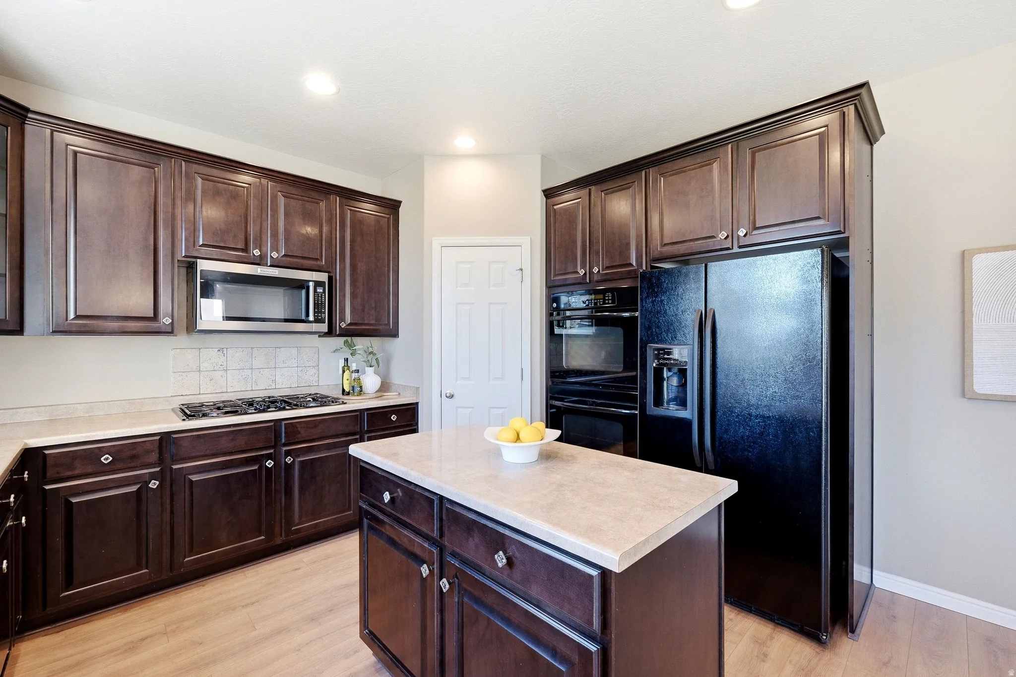 Spacious kitchen featuring dark wood cabinetry, a central island with countertop, stainless steel microwave, gas cooktop, and wood-finish flooring