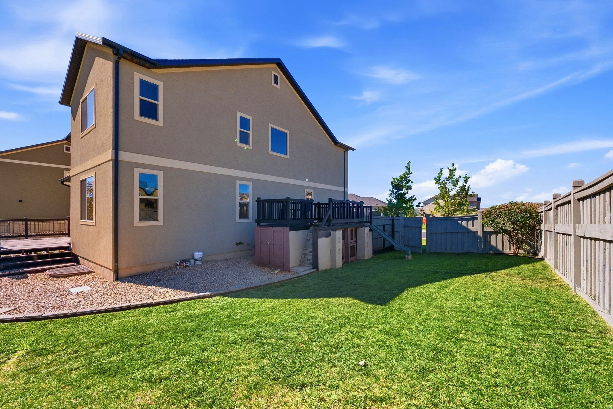 Expansive backyard featuring a manicured lawn, gravel landscaping, a privacy fence, and a multi-level deck