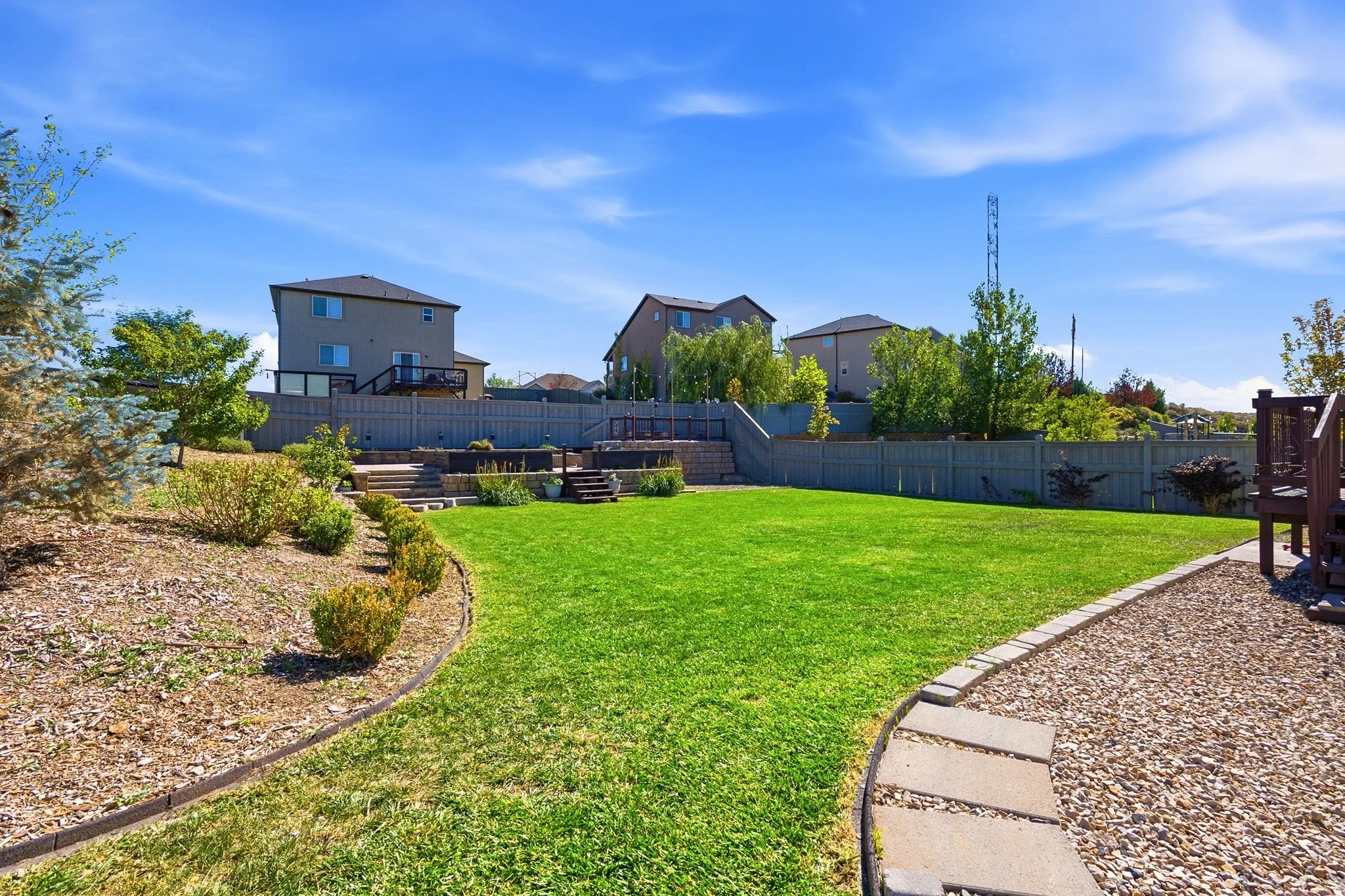 Expansive backyard featuring a manicured lawn, tiered landscaping, and a multi-level deck