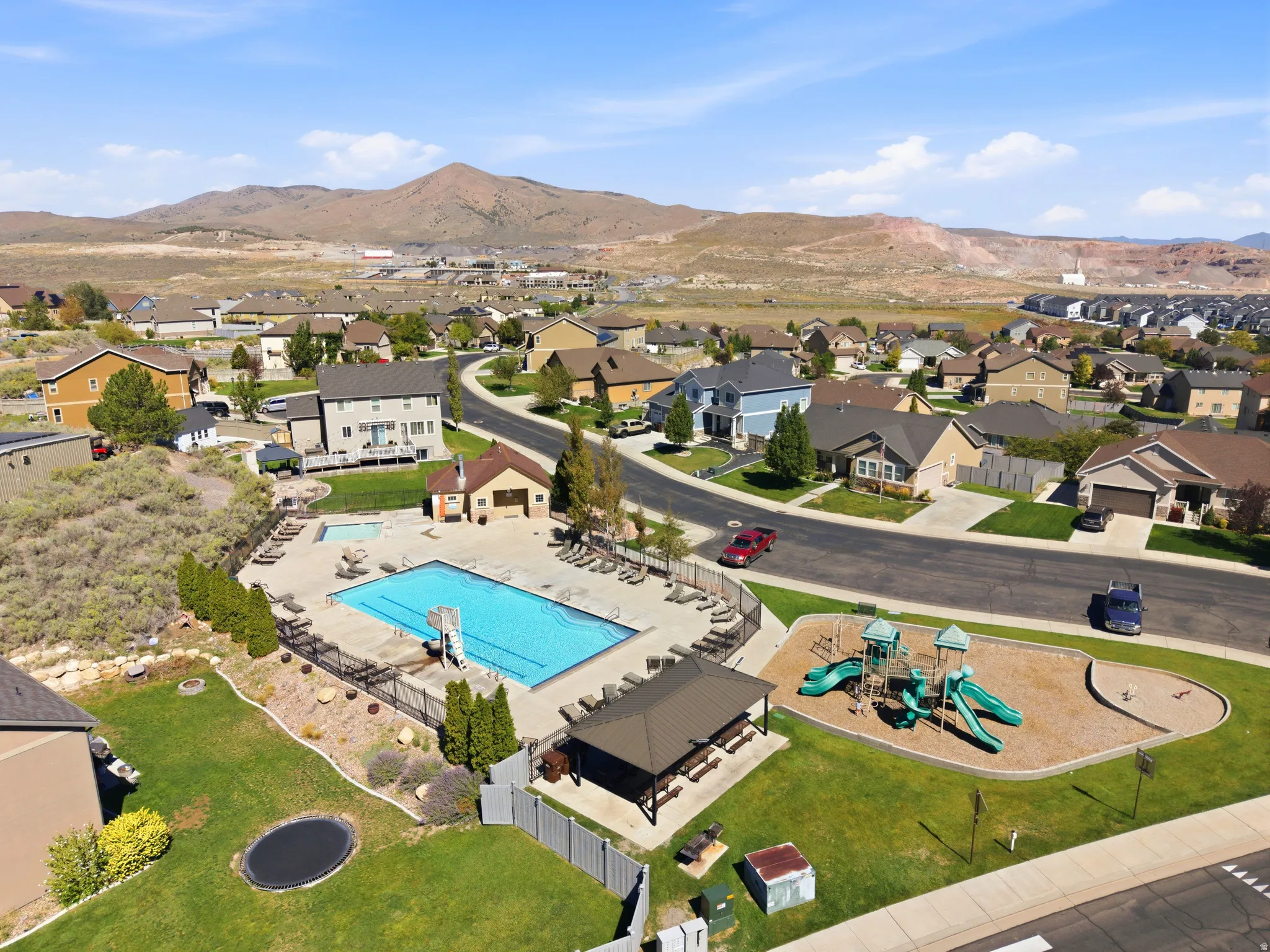 Community swimming pool, adjacent recreational play structure, covered outdoor seating area, manicured lawns, and surrounding residential properties